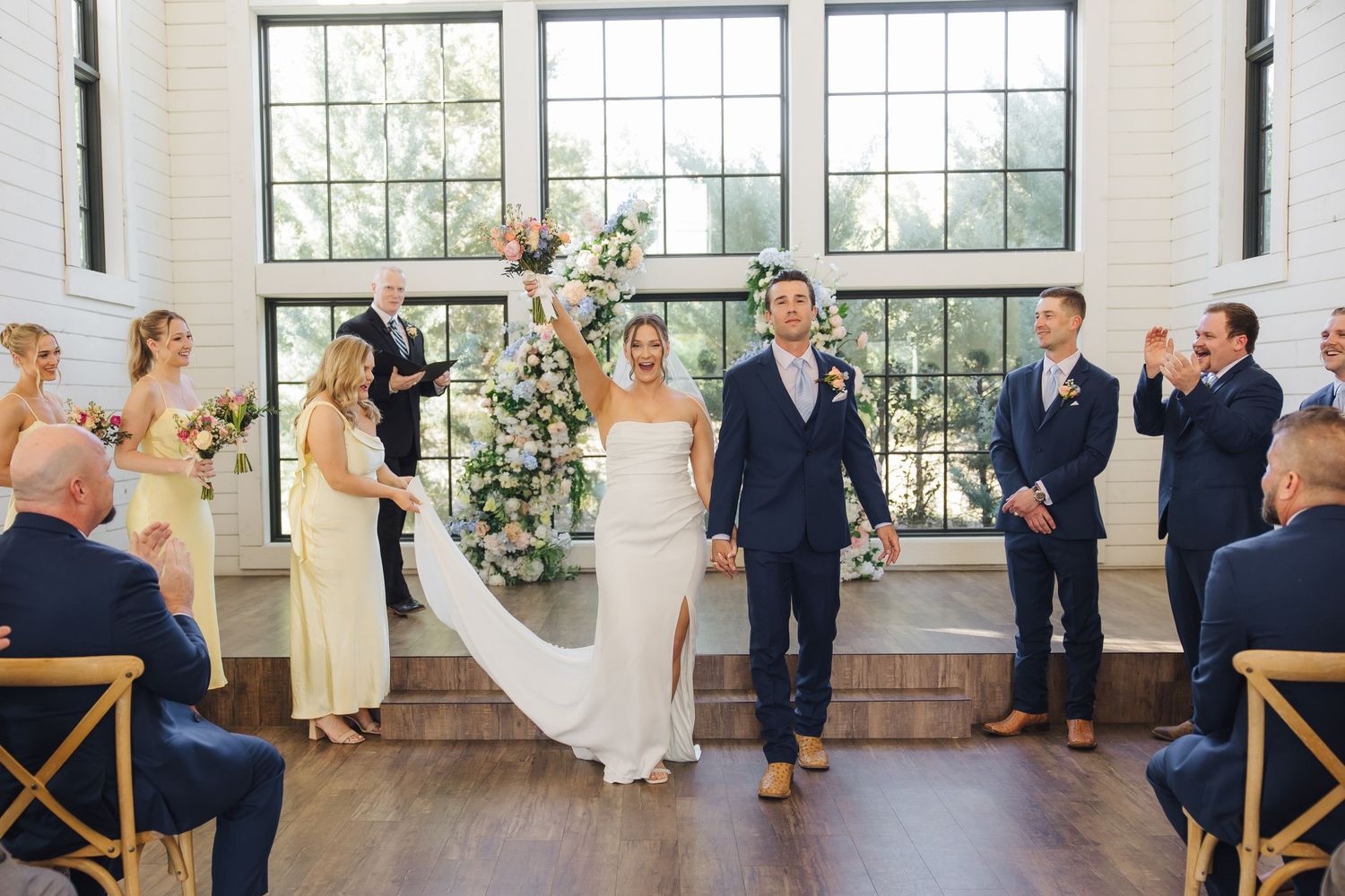 A joyful celebration during a wedding ceremony in a bright industrial venue with large windows and wooden floors.