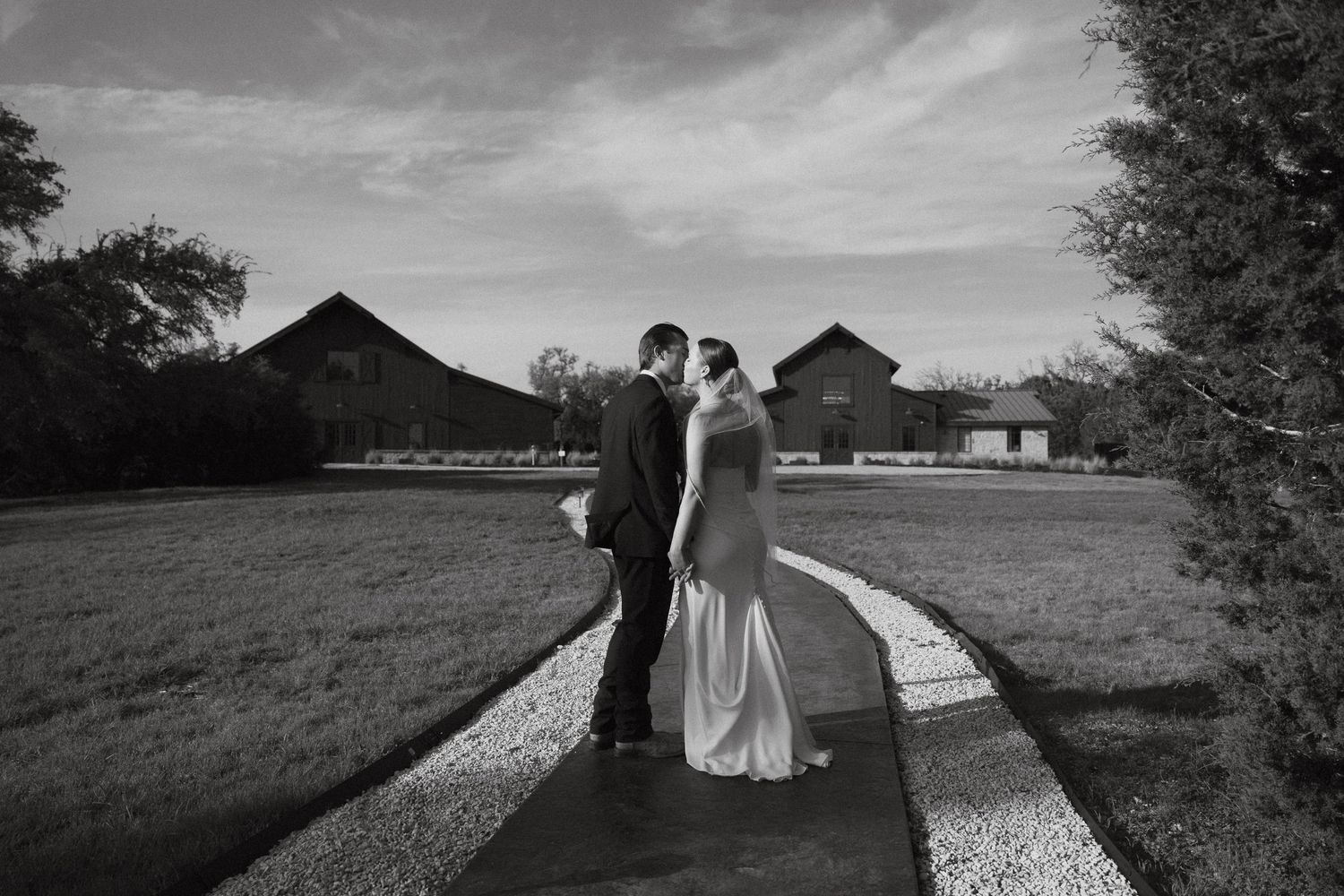 A dramatic black and white wedding scene with silhouettes walking along a country path against a cloudy sky.