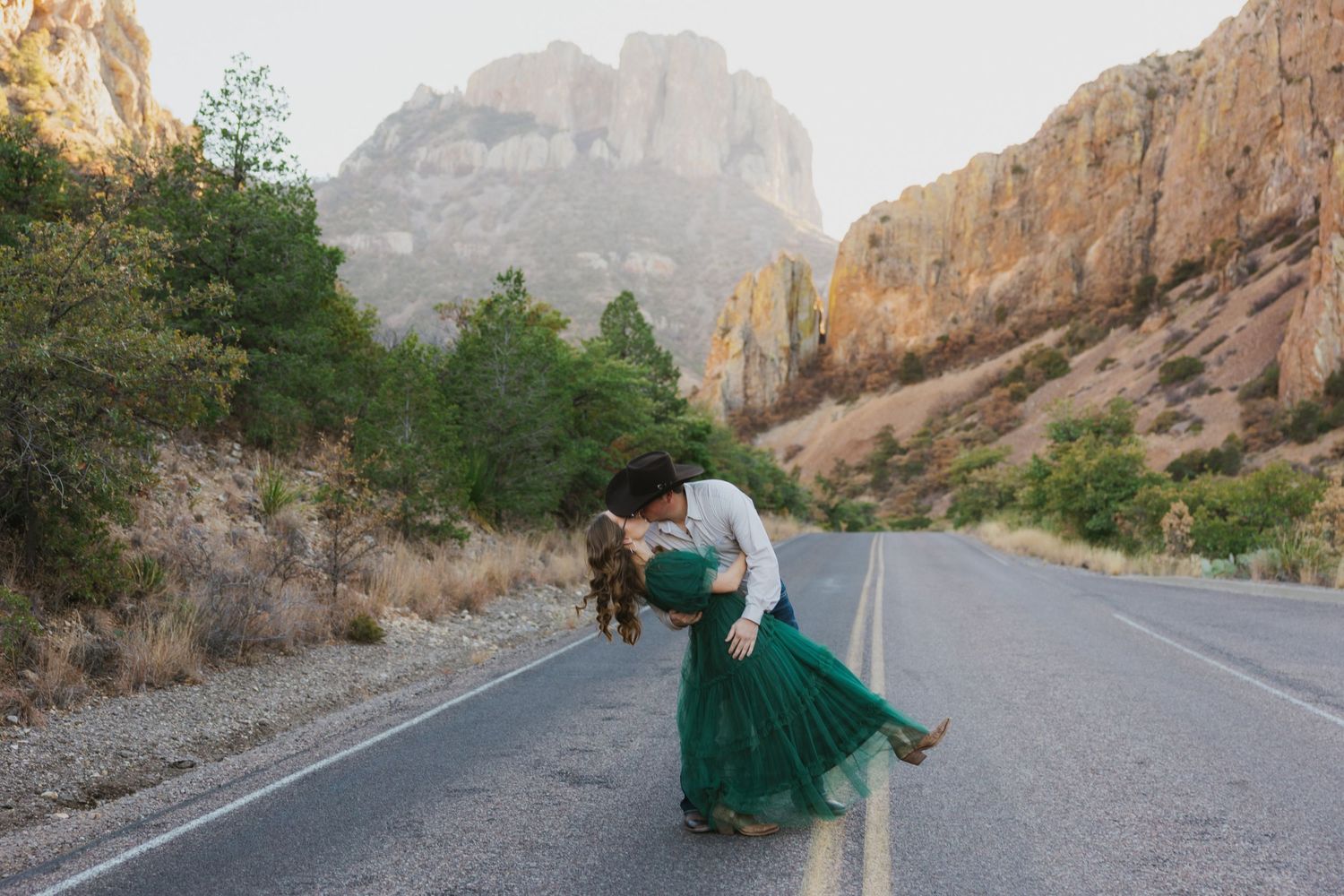 Two people dancing together in an intimate pose on a mountain road with dramatic cliffs in the background.