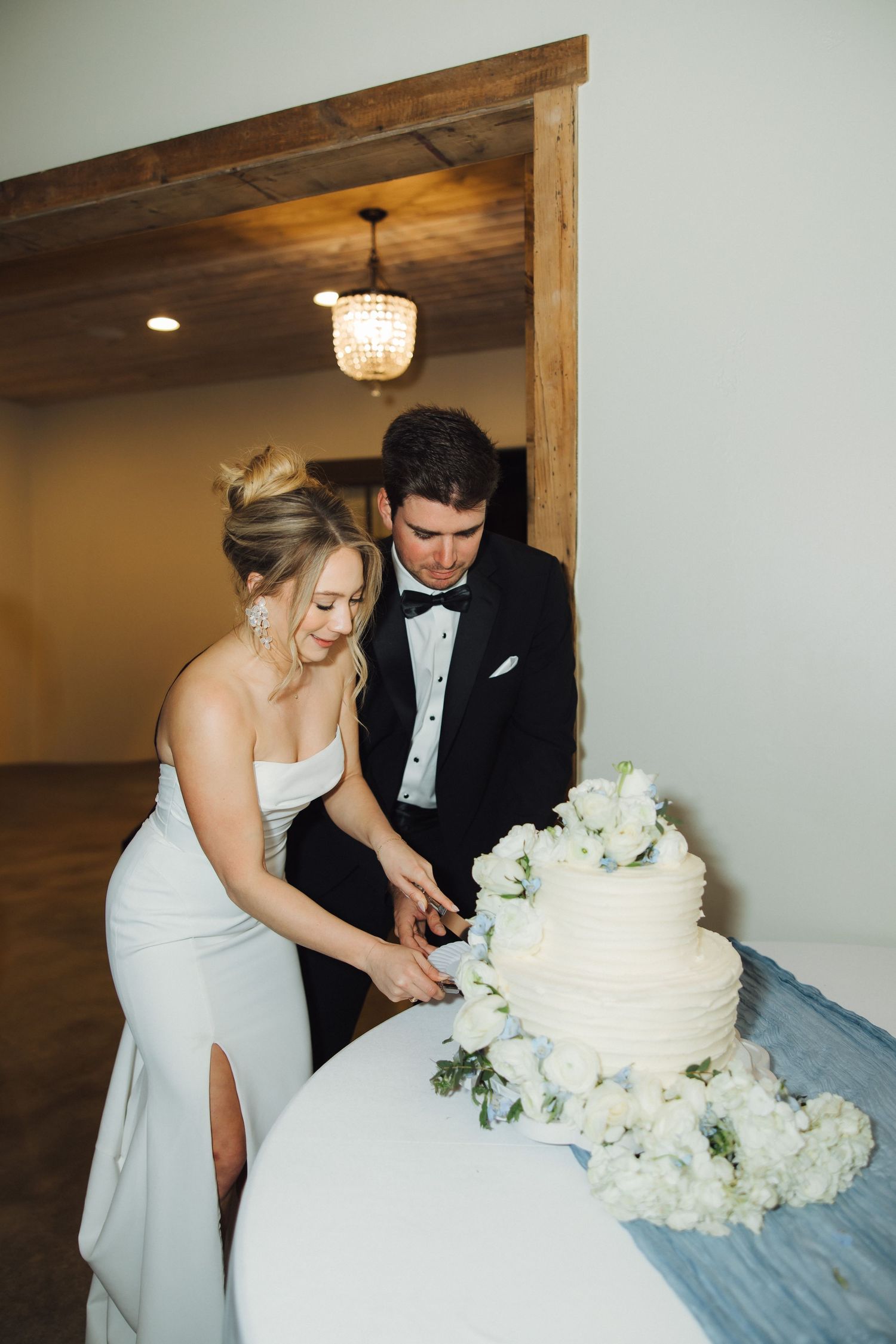 Wedding cake cutting sequence showing elegant white tiered cake with floral decorations on blue tablecloth.