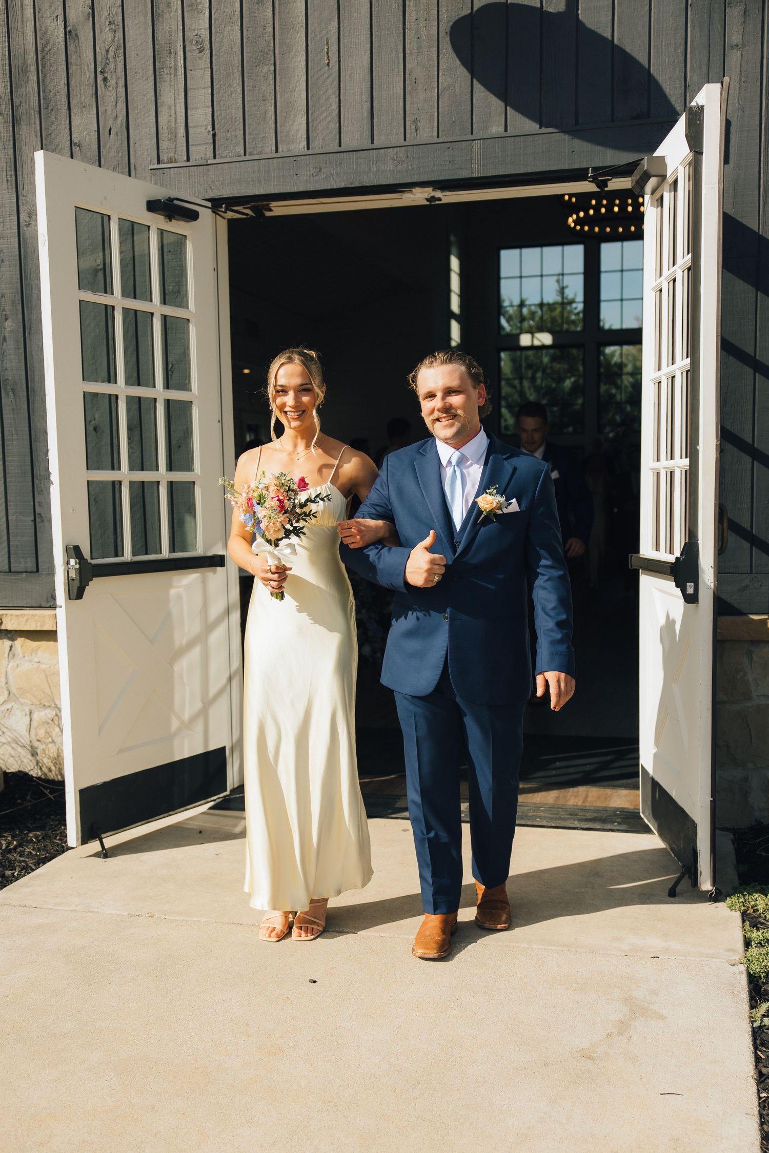 Couple walking outdoors on a paved pathway near a building with large windows and French doors.