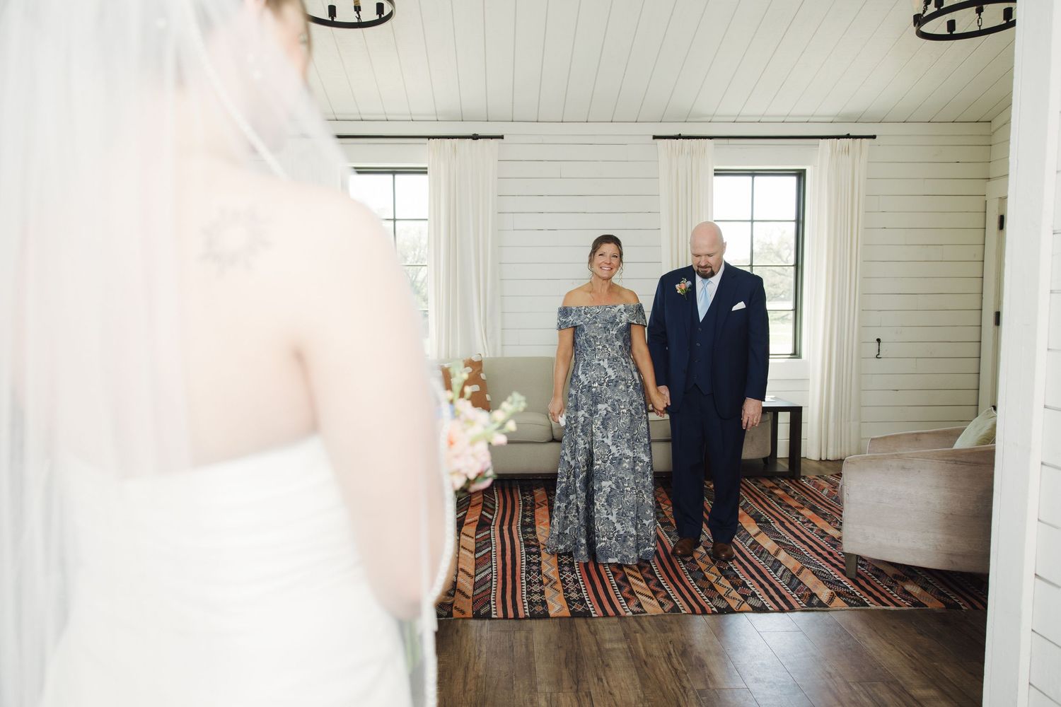Emotional first look moment at a rustic white chapel venue with striped rug and natural lighting through windows.
