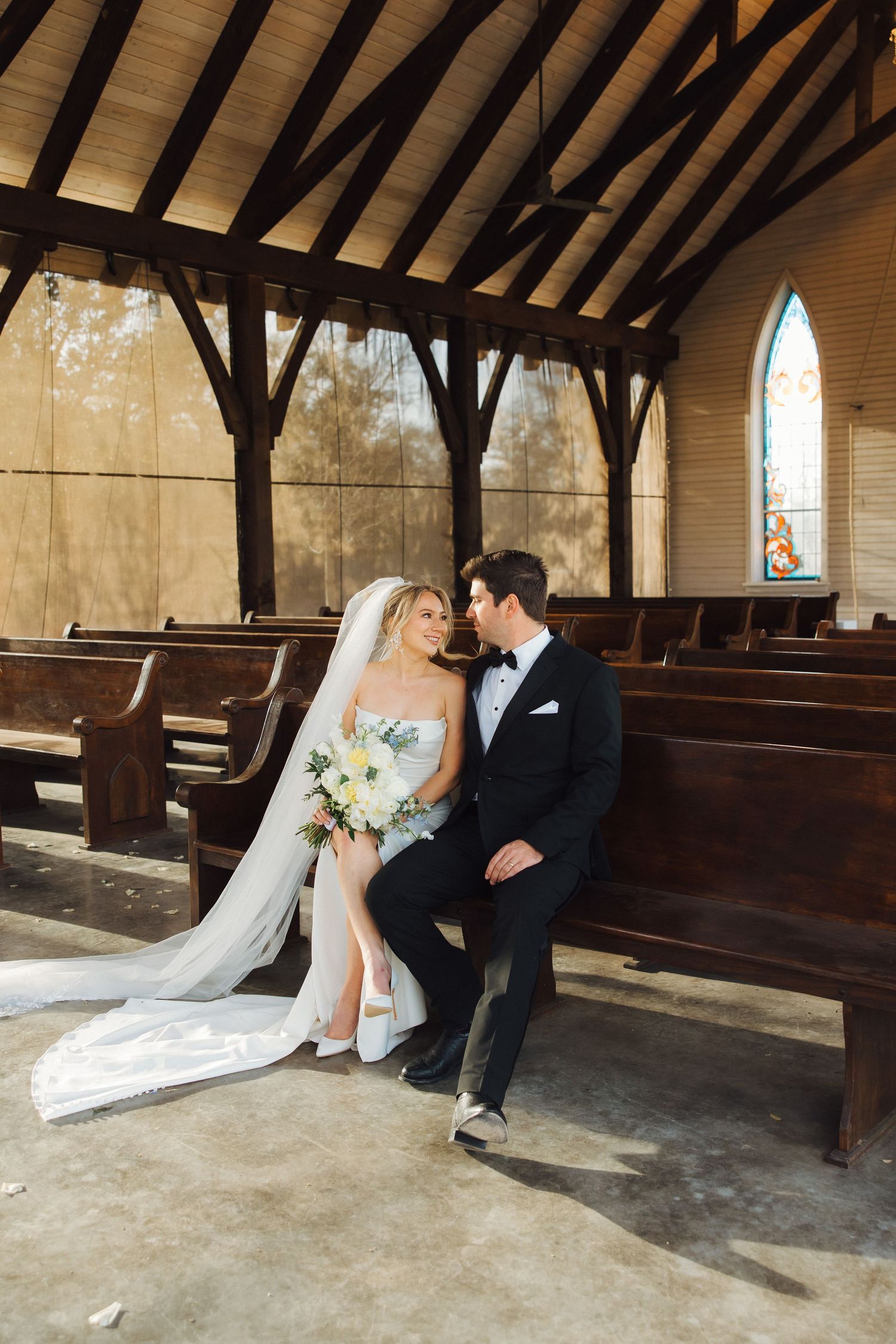 A romantic wedding moment inside a rustic chapel with wooden beams and stained glass windows.