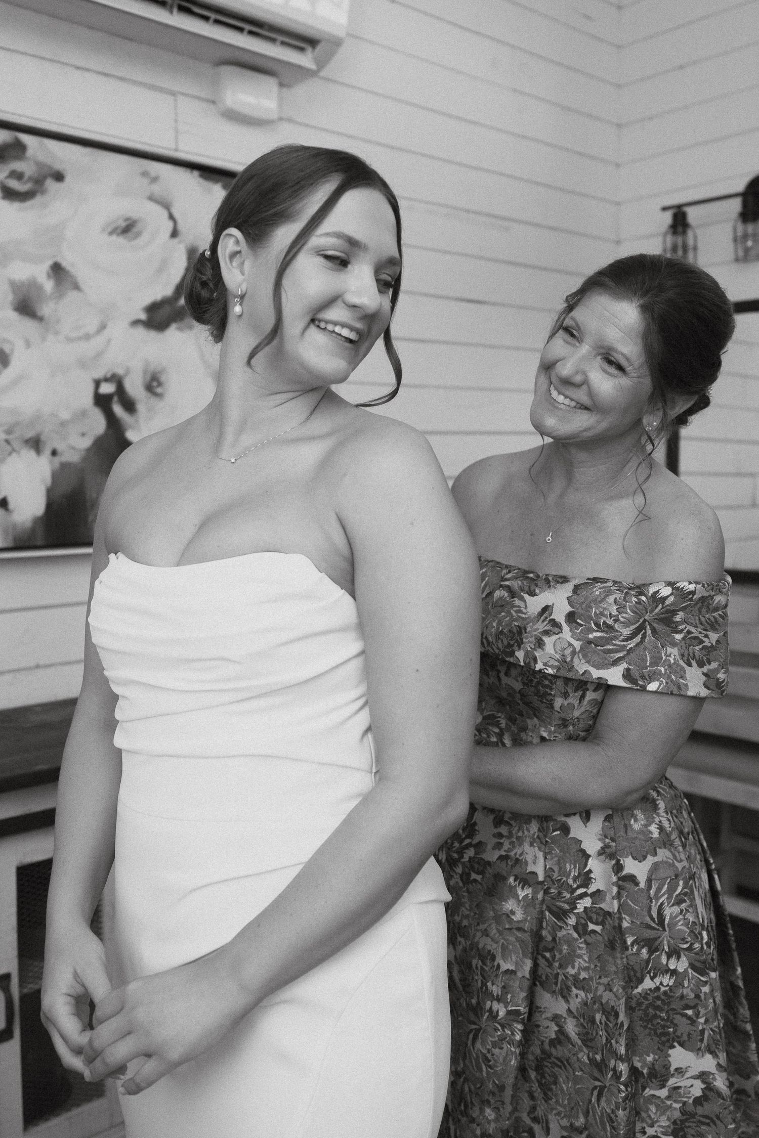 Black and white photo showing two women sharing a candid joyful moment during a wedding getting ready moment.