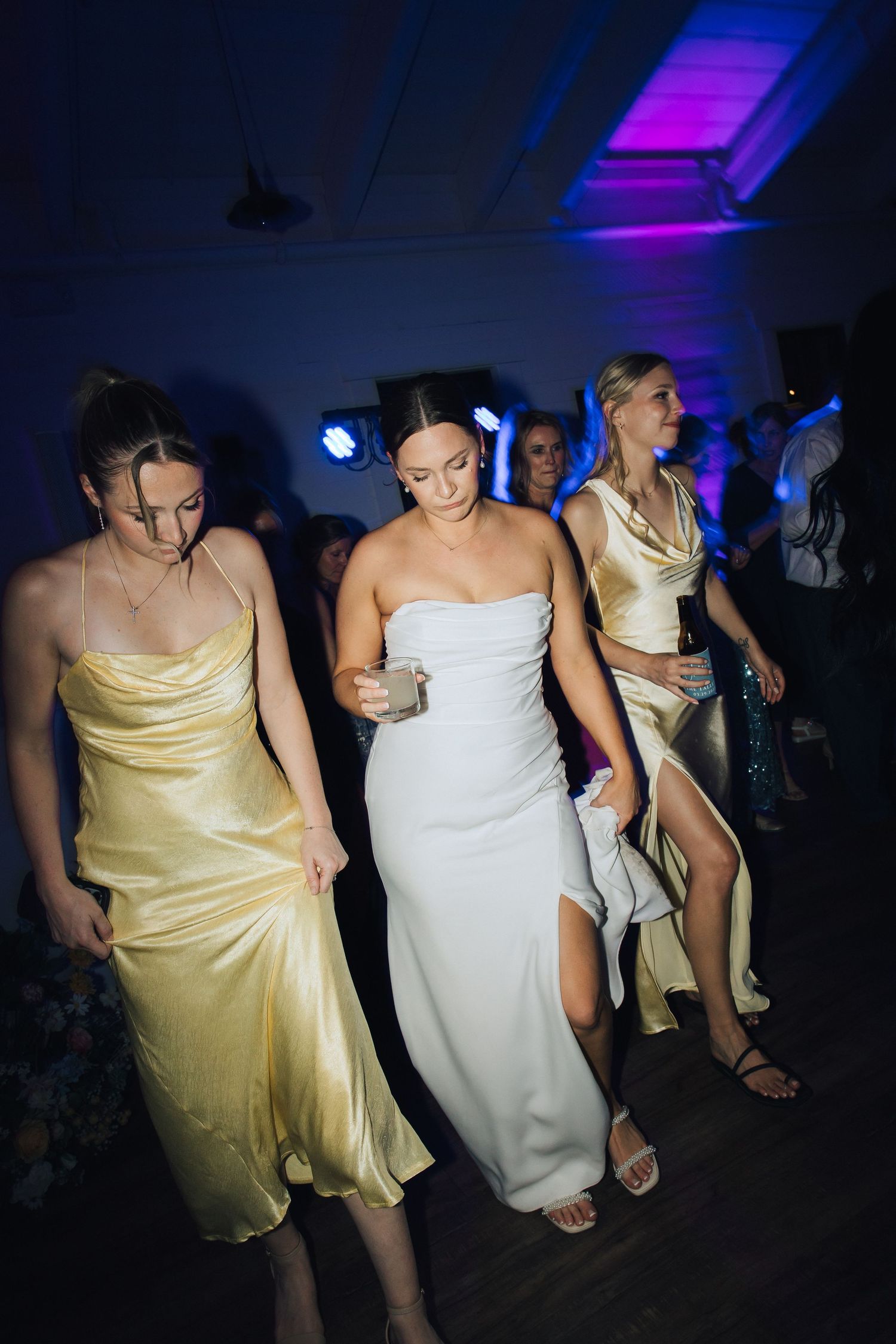 Wedding guests dancing on a dark dance floor with colorful blue and purple lighting overhead.