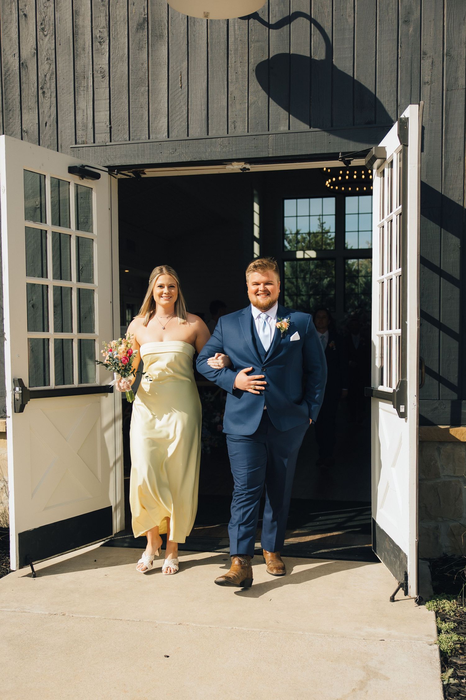 A couple exits through white doors of a modern barn venue on their wedding day.