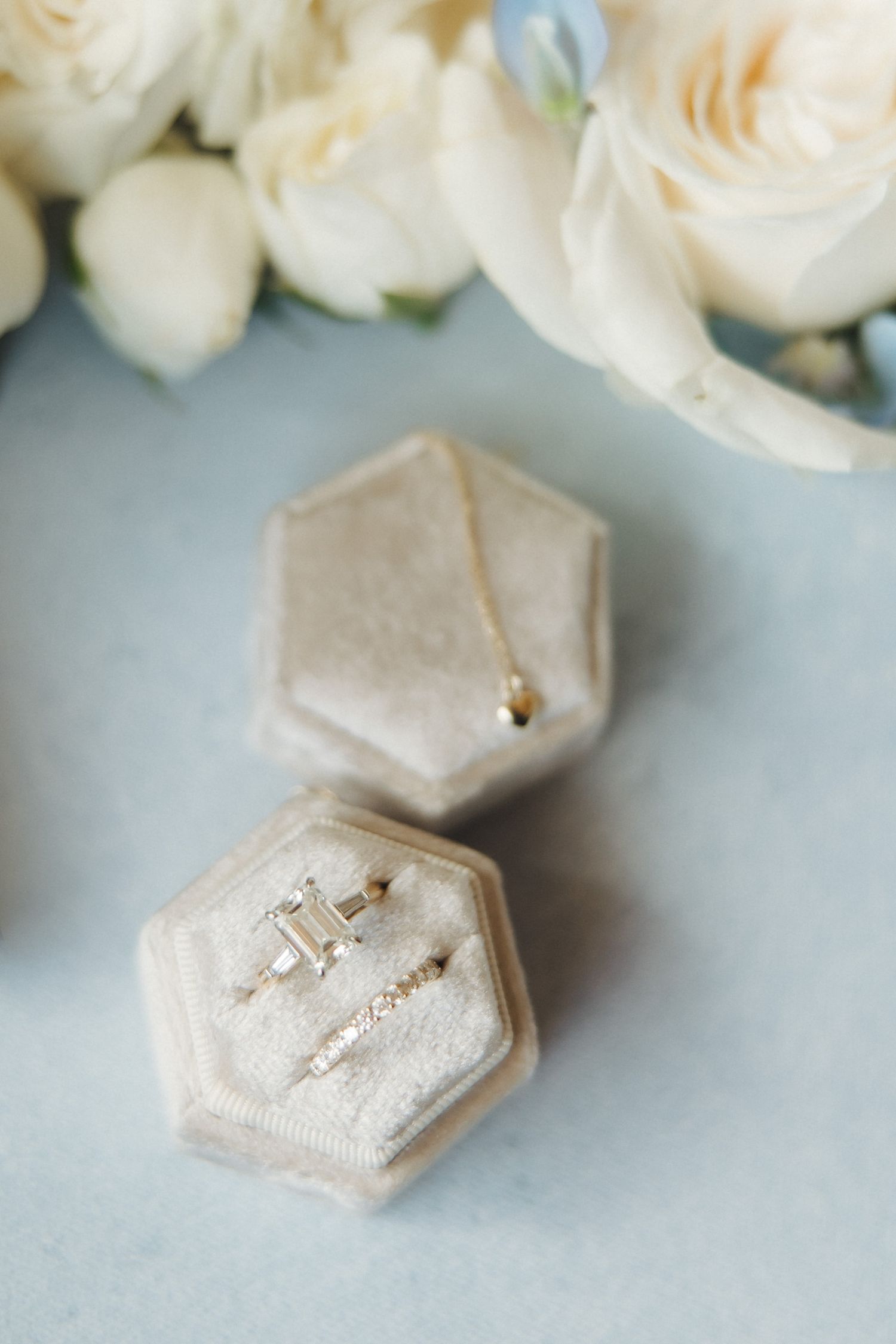 Delicate hexagonal velvet ring boxes with sparkly jewelry pieces displayed with soft white roses in the background.