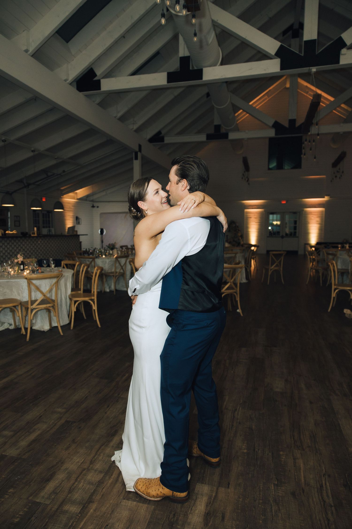 A couple shares a passionate dance embrace on a dark wooden floor in an elegant venue with vaulted ceilings.