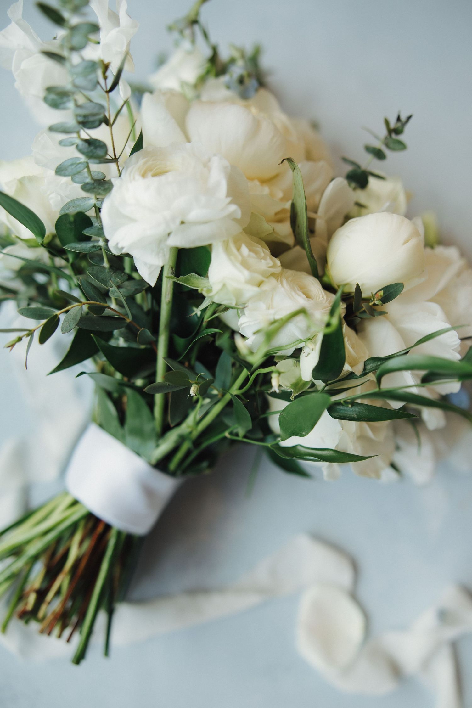 Classic white rose and eucalyptus bridal bouquet wrapped with ribbon against a light blue background.