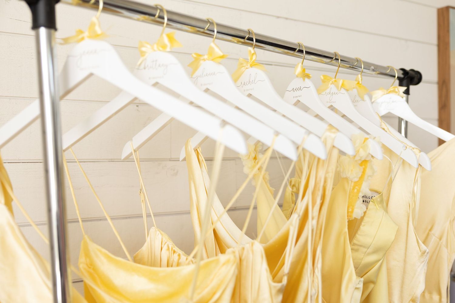 White plastic hangers holding pale yellow formal dresses arranged in a row on a metal clothing rack.