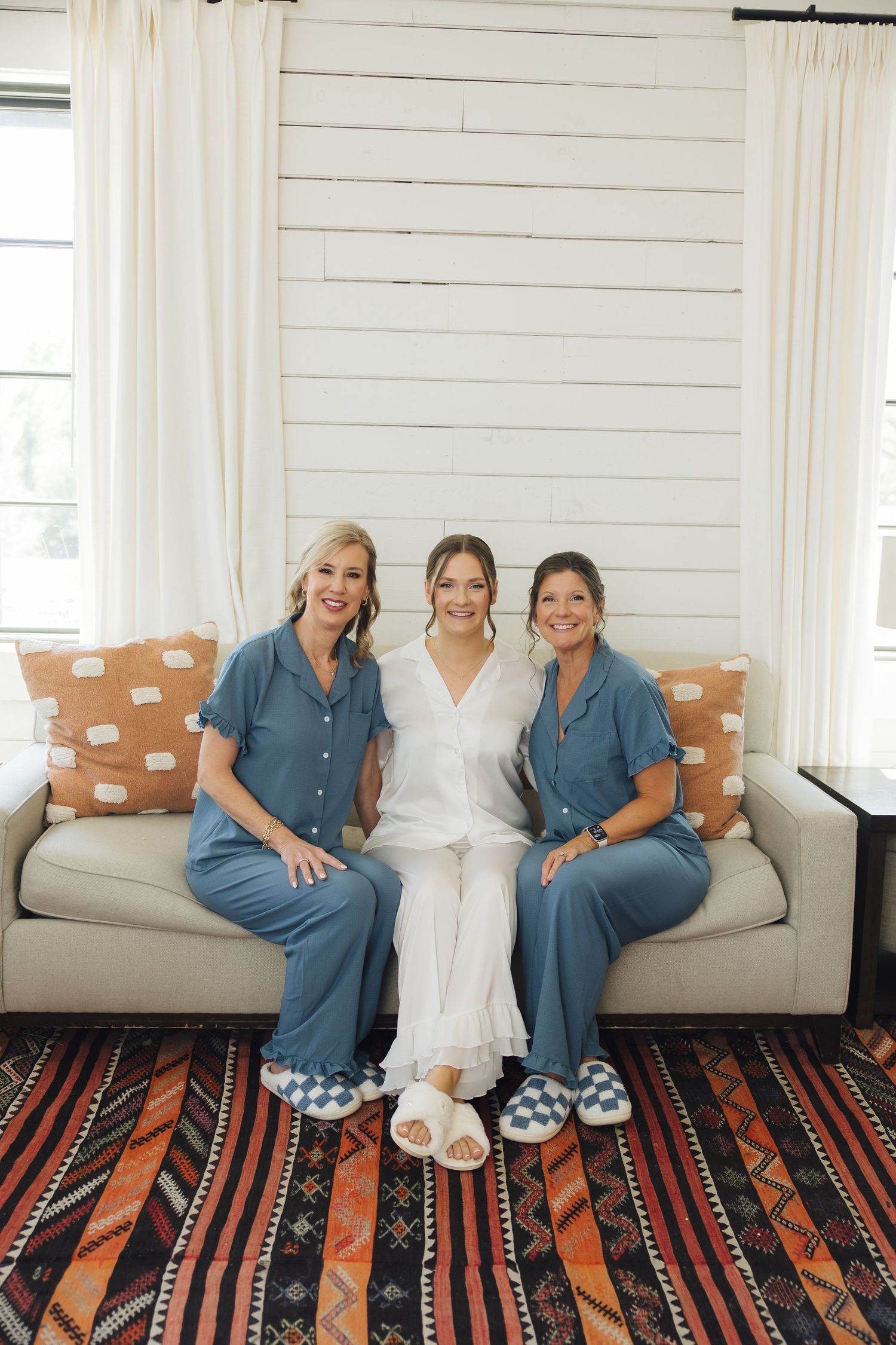 Four people sit on a cream couch wearing matching blue outfits and slippers against white shiplap walls.