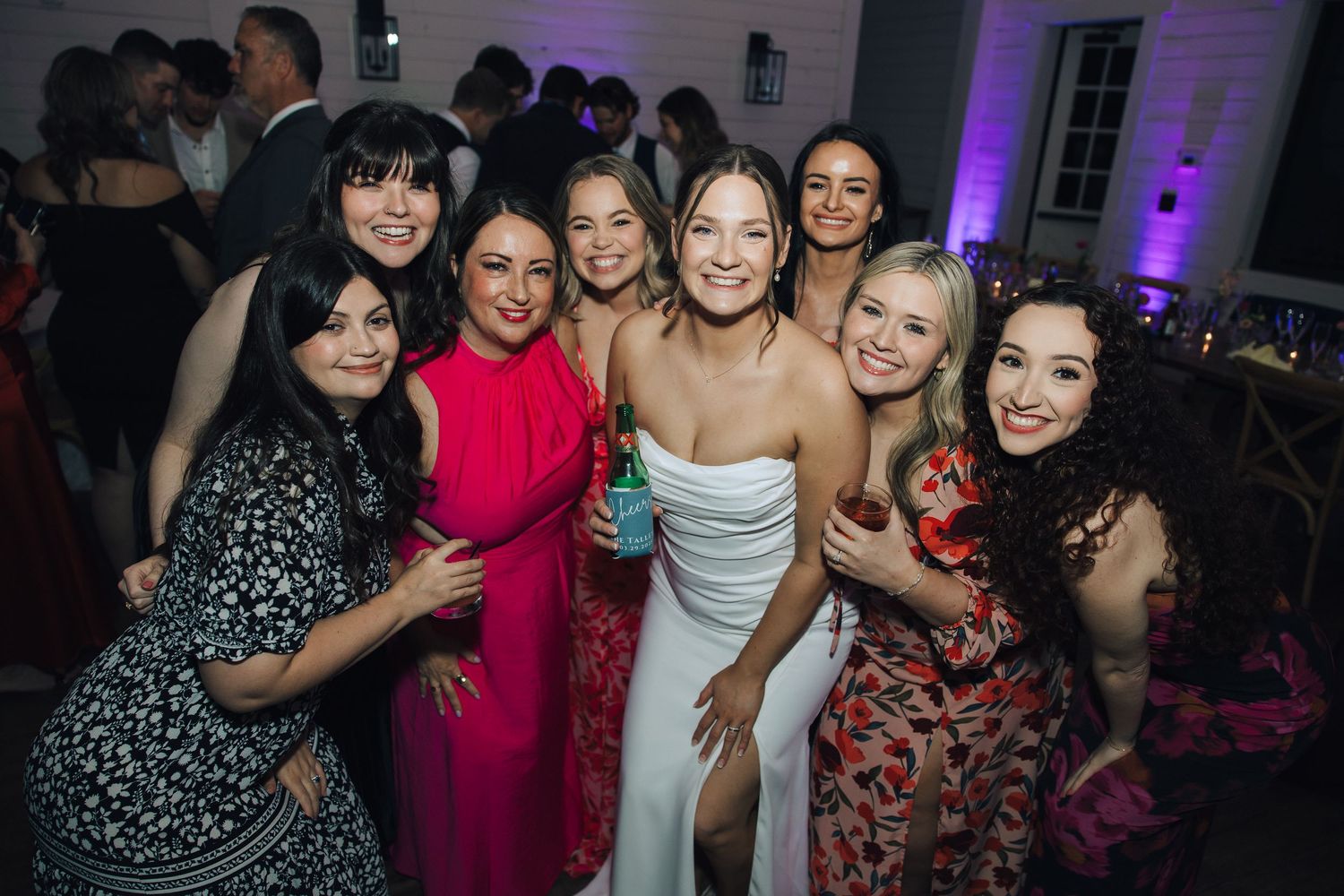 A group of party guests dancing and socializing at a colorful evening celebration with purple lighting.