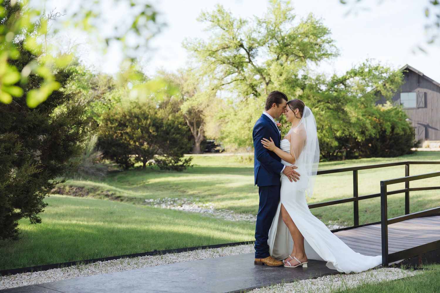 A couple in wedding attire embraces on a rustic wooden bridge nestled in lush green surroundings on their special day.