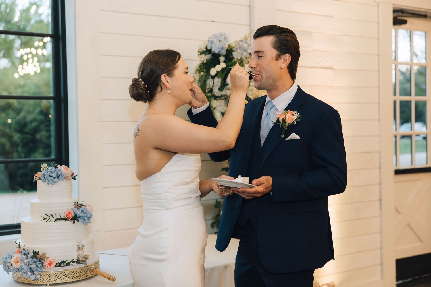 A newlywed couple shares wedding cake during their reception in front of a tiered blue and white cake.