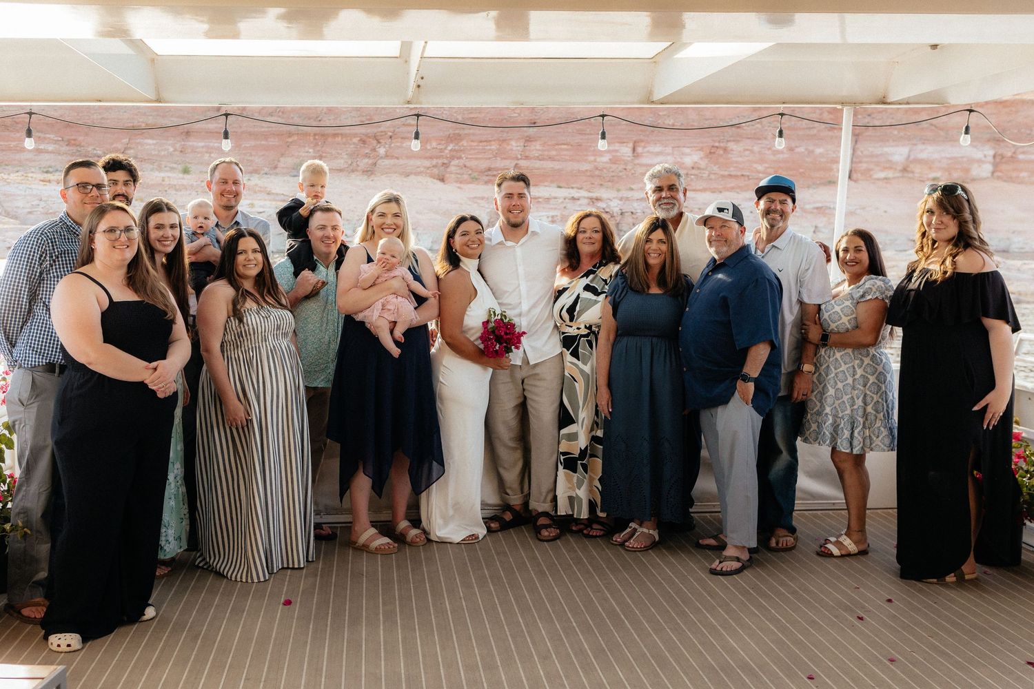 A panoramic collage shows a large wedding party posing together against a rustic brick wall with hanging string lights.