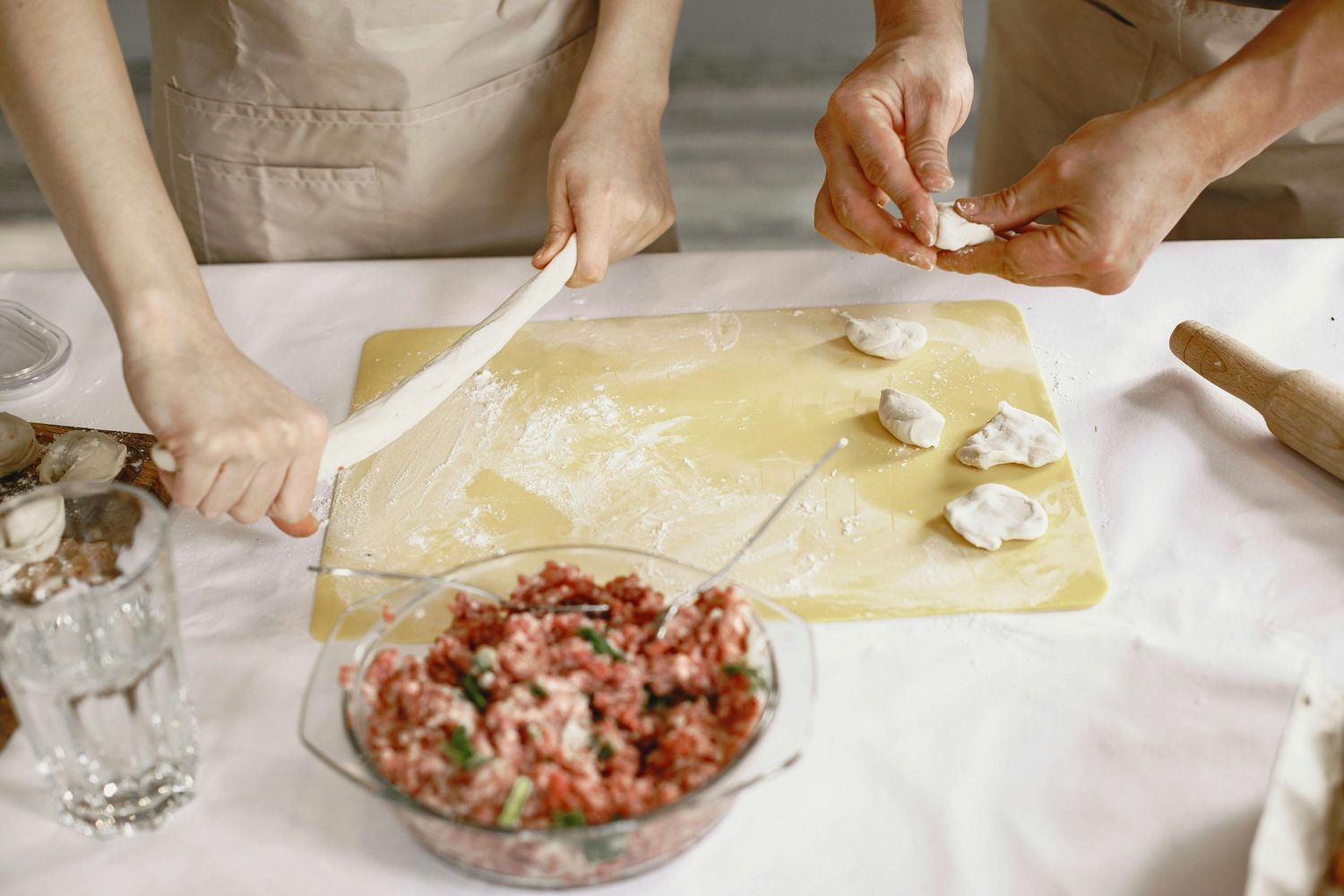 Hands preparing homemade ravioli with pasta dough and a bowl of fresh filling on a white table.
