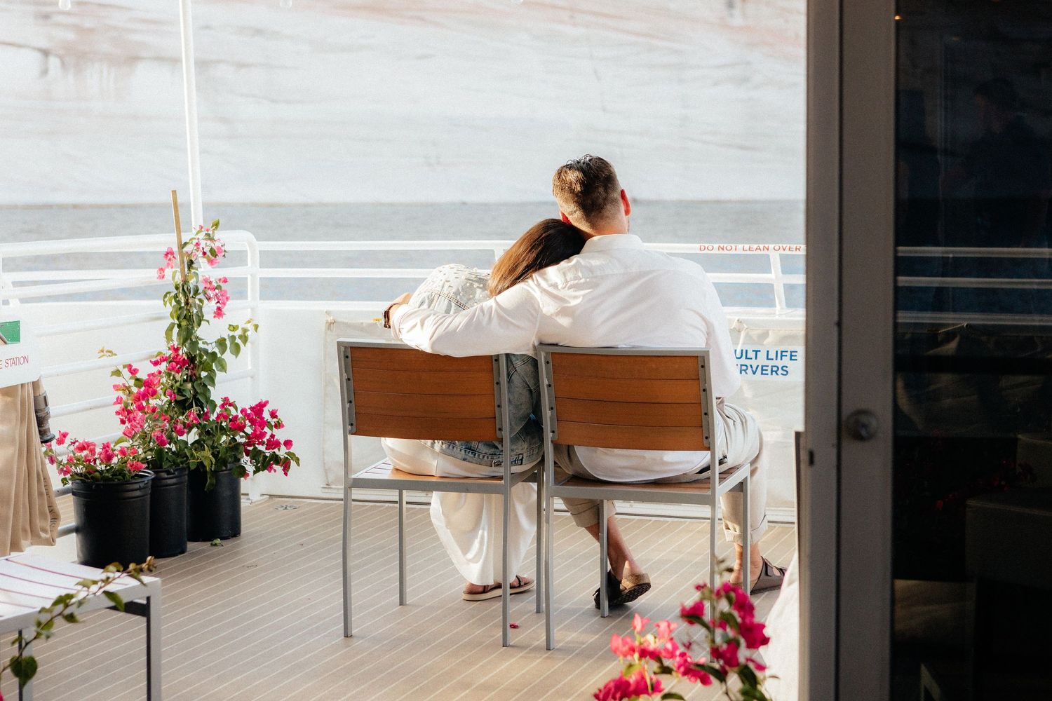 A modern minimalist interior space with wooden chairs and pink flowers in planters near large windows.