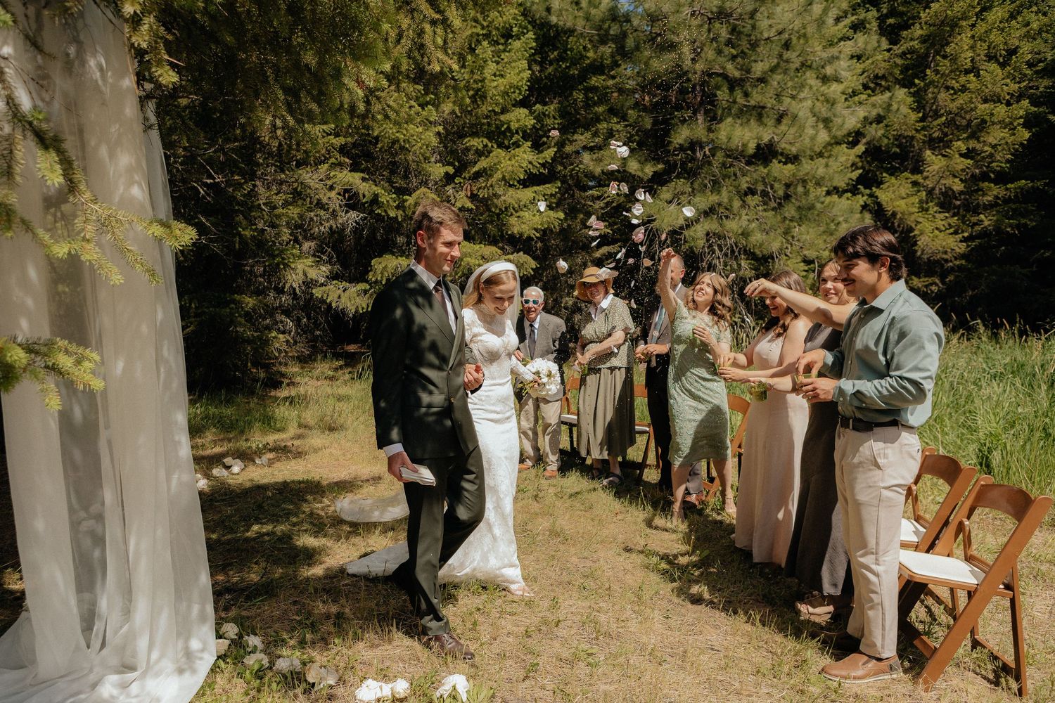 Wedding ceremony takes place on forest path with wedding party lined up under trees in natural outdoor setting.