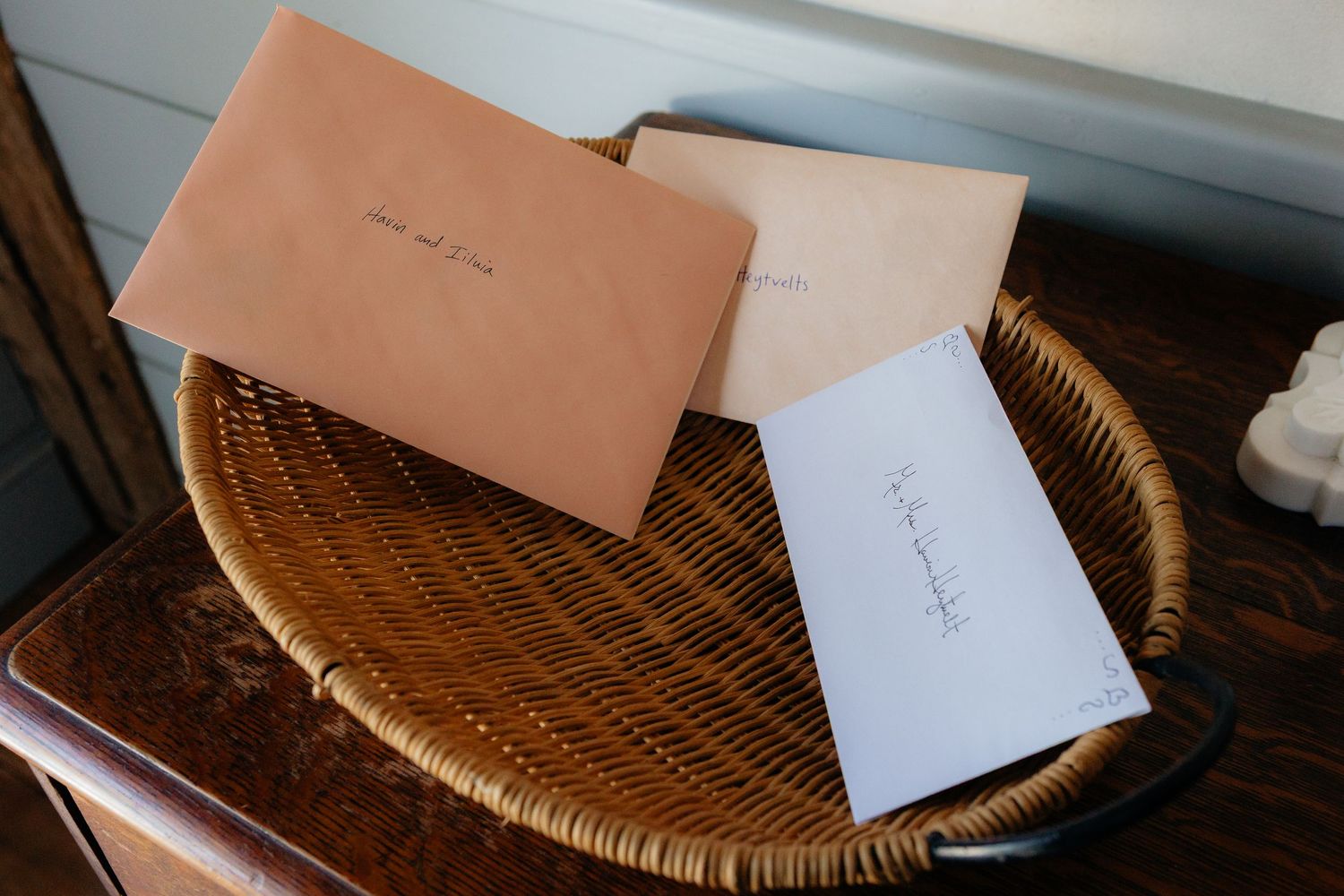 Three simple envelopes in peach and white colors rest on a woven wicker tray.