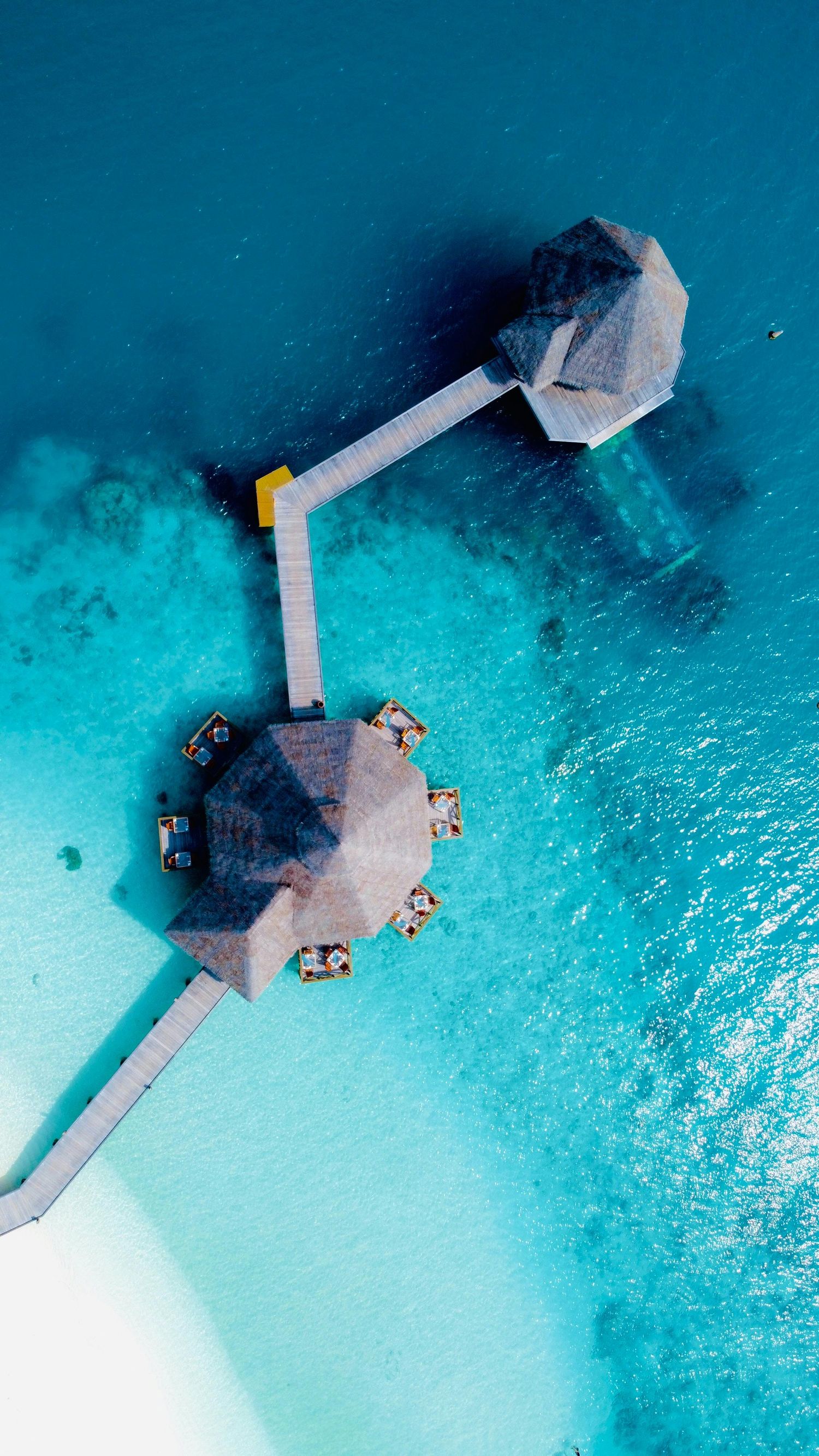 Aerial view of overwater bungalows connected by walkways in crystal clear turquoise tropical waters.