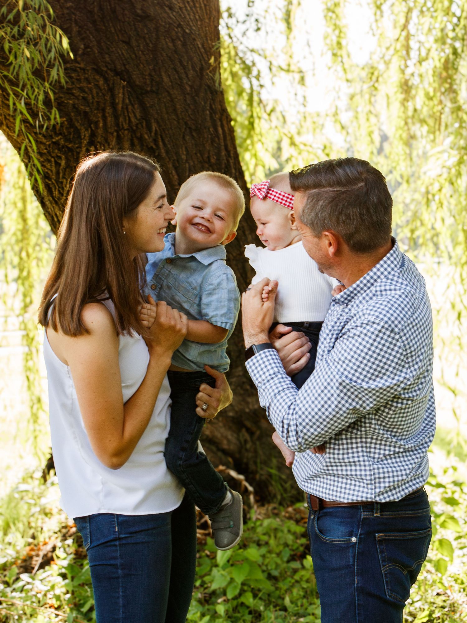 Happy family sharing joyful moment under a willow tree in sunlit park.