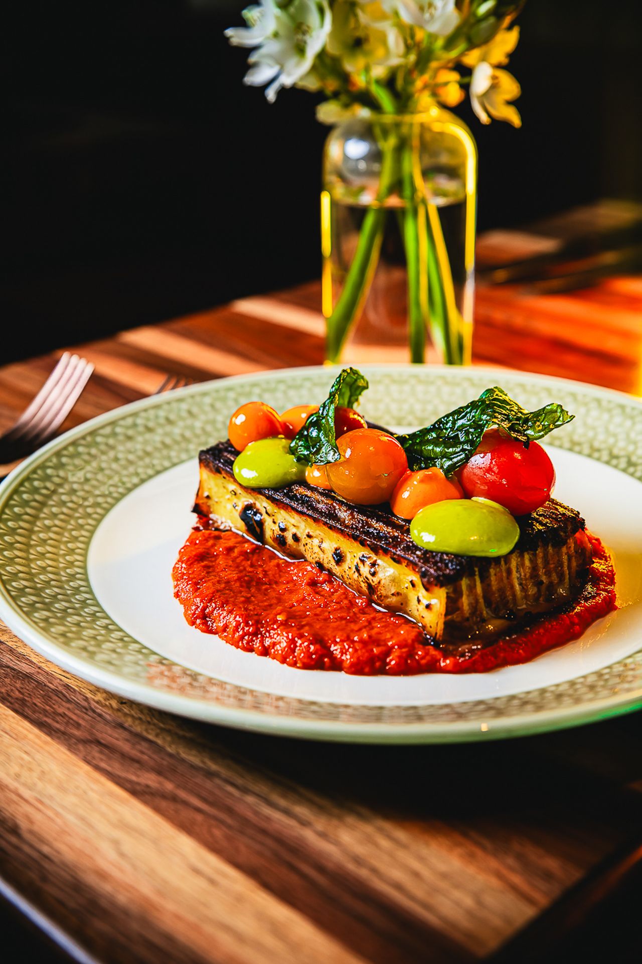 Beautifully plated vegetable dish with colorful tomatoes and red sauce on green ceramic plate.