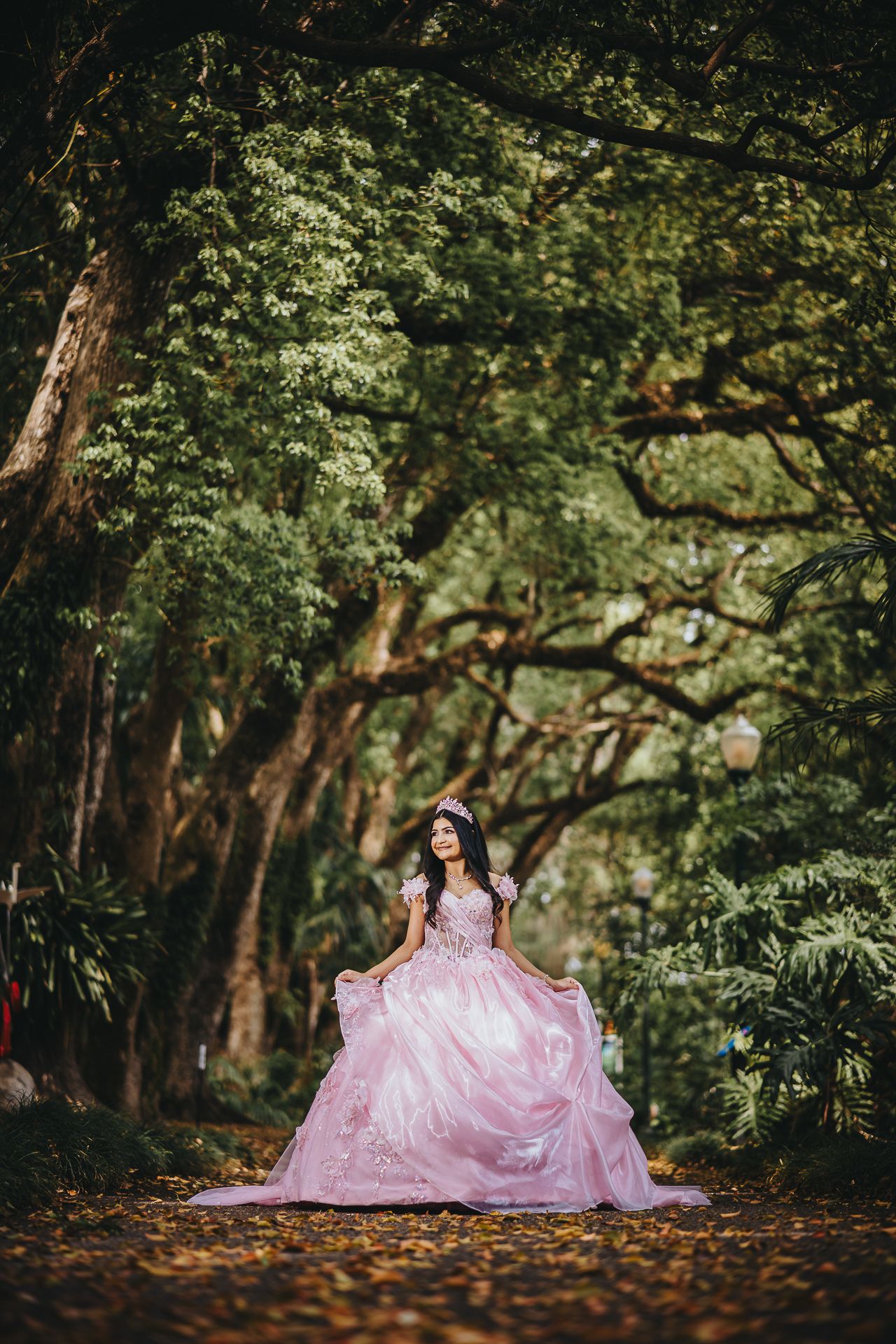 Person wearing pink princess gown poses in magical forest setting.