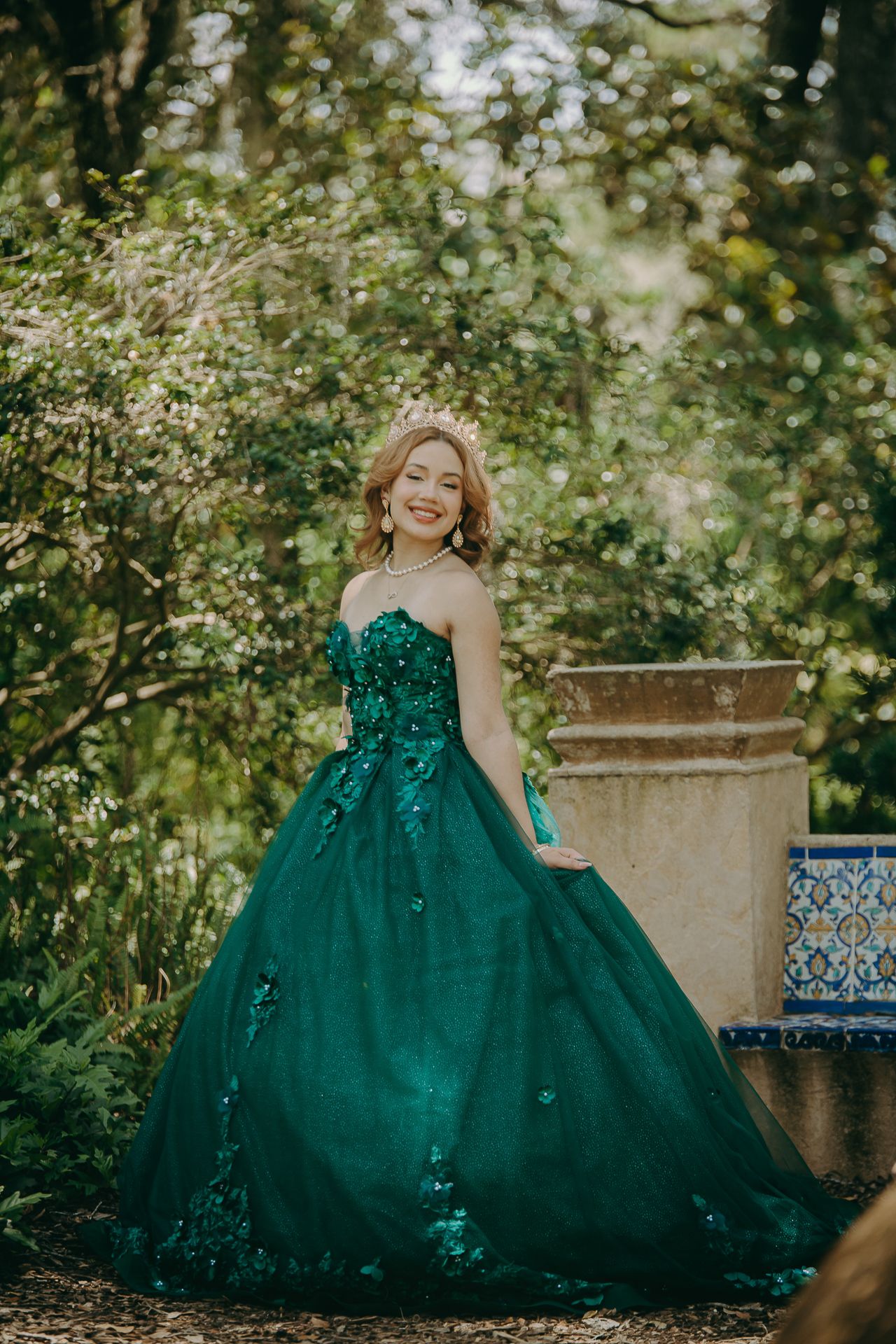 A elegant emerald green ball gown with sparkle details photographed in a lush garden setting with soft natural lighting.
