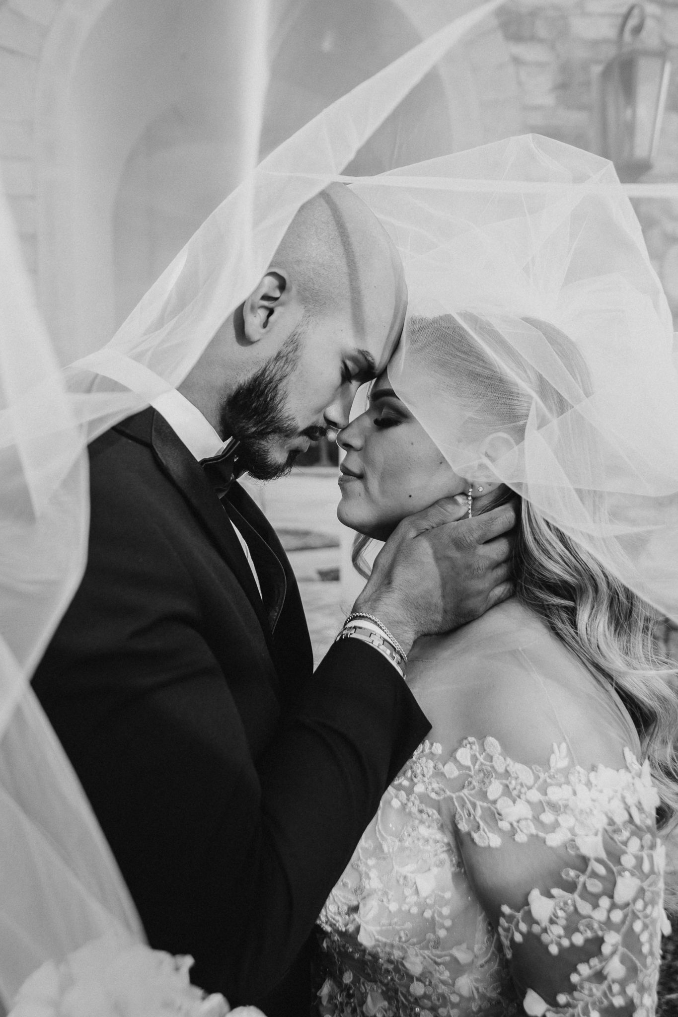 A tender black and white romantic moment under a flowing veil between newlyweds on their wedding day.