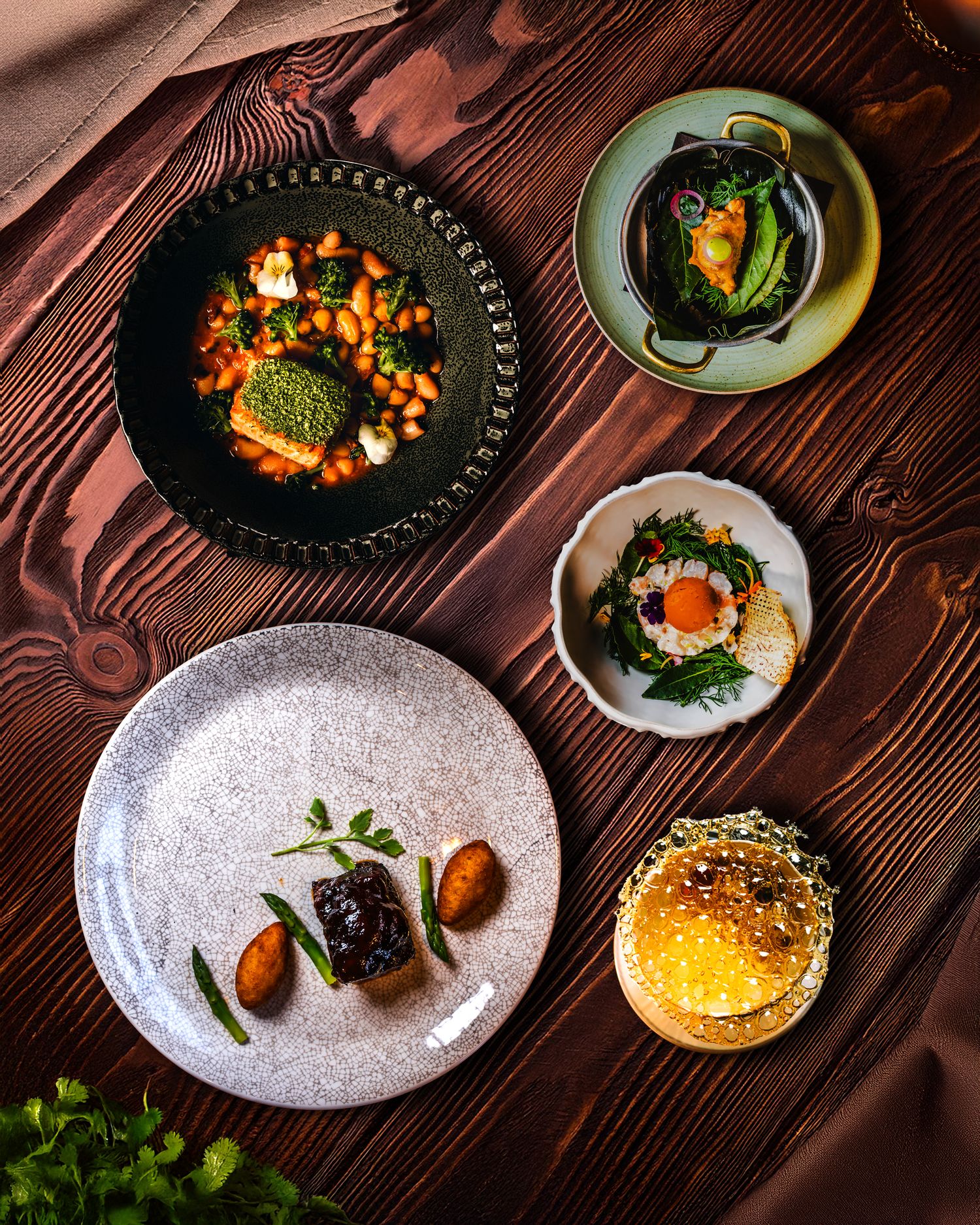 Overhead view of modern plated dishes featuring colorful sauces and garnishes on dark wooden table.