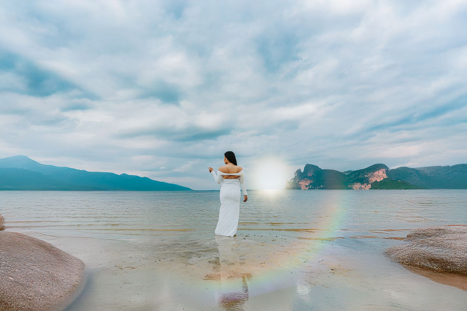 A dreamy scene at a lakeside beach with a figure in white dress standing against mountain backdrop and lens flare.