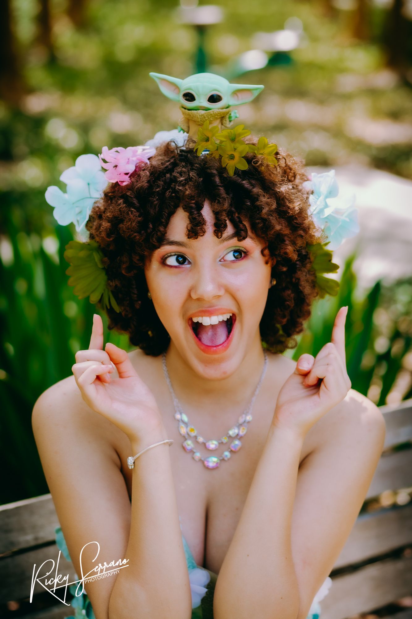 Playful portrait in garden setting with Baby Yoda toy and floral accessories glowing in natural sunlight.