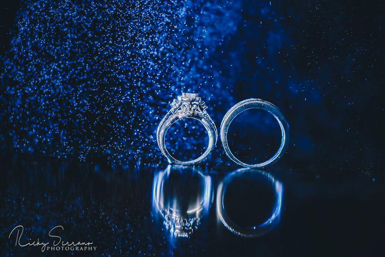 Wedding rings with sparkly blue reflection creating artistic jewelry photography.