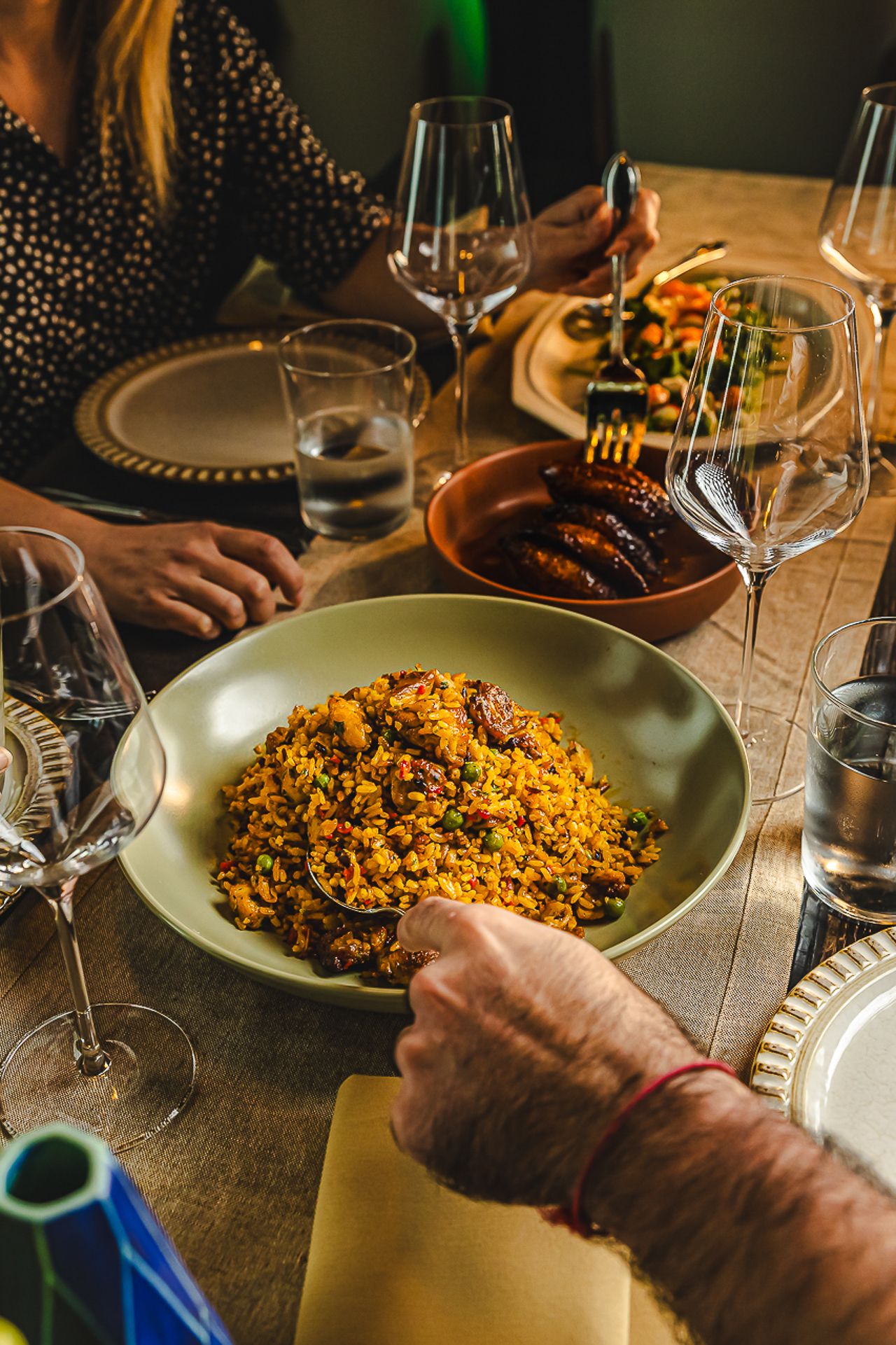 Dining table with yellow rice dish and wine glasses in warm ambient restaurant lighting.