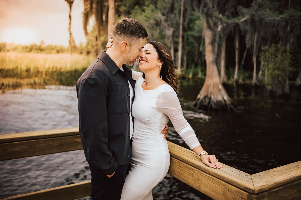 A romantic couple shares an intimate moment on a wooden dock by a lake during golden hour.