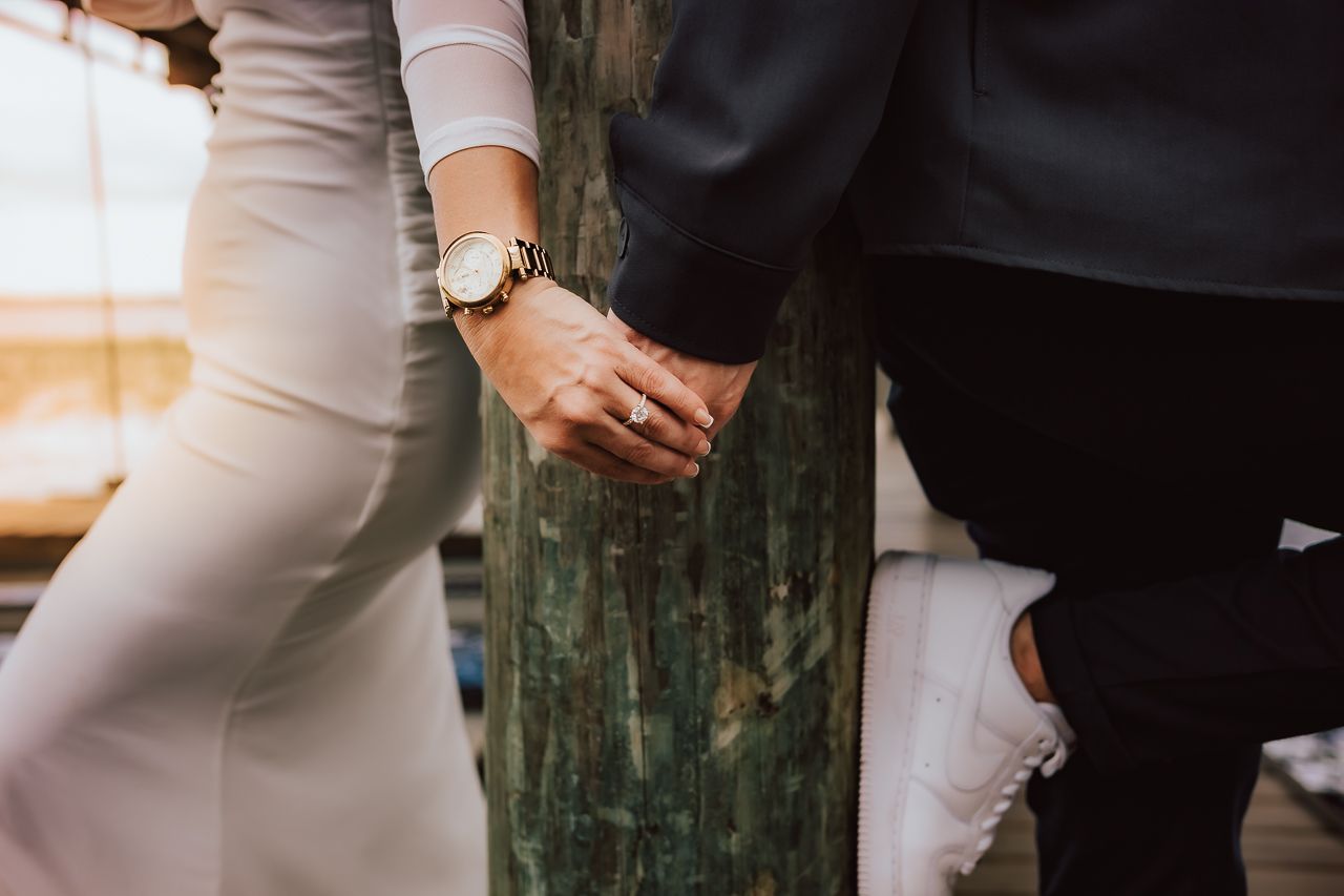 Close-up view of two people holding hands near a green wooden post, wearing contrasting light and dark outfits.