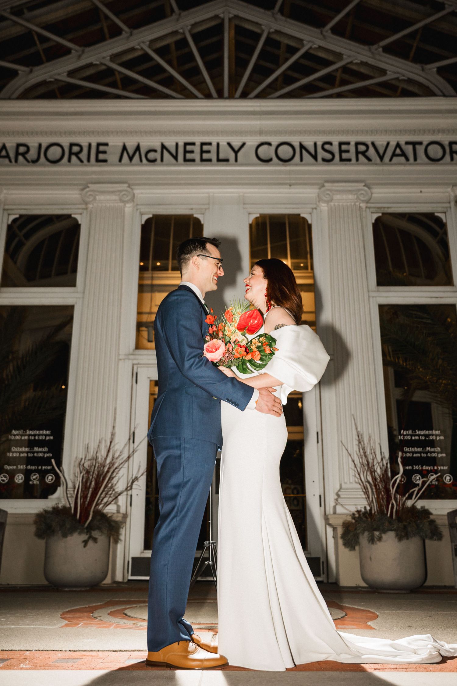 A wedding couple sharing an intimate moment outside the Marjorie McNeely Conservatory at night.