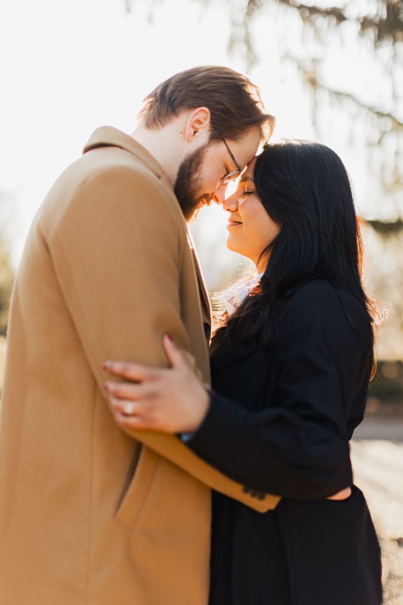 Couple in warm embrace sharing intimate moment under willow trees at sunset.