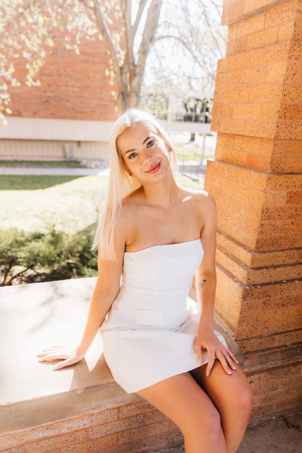 Candid graduation photos captured in natural sunlight by brick pillars.