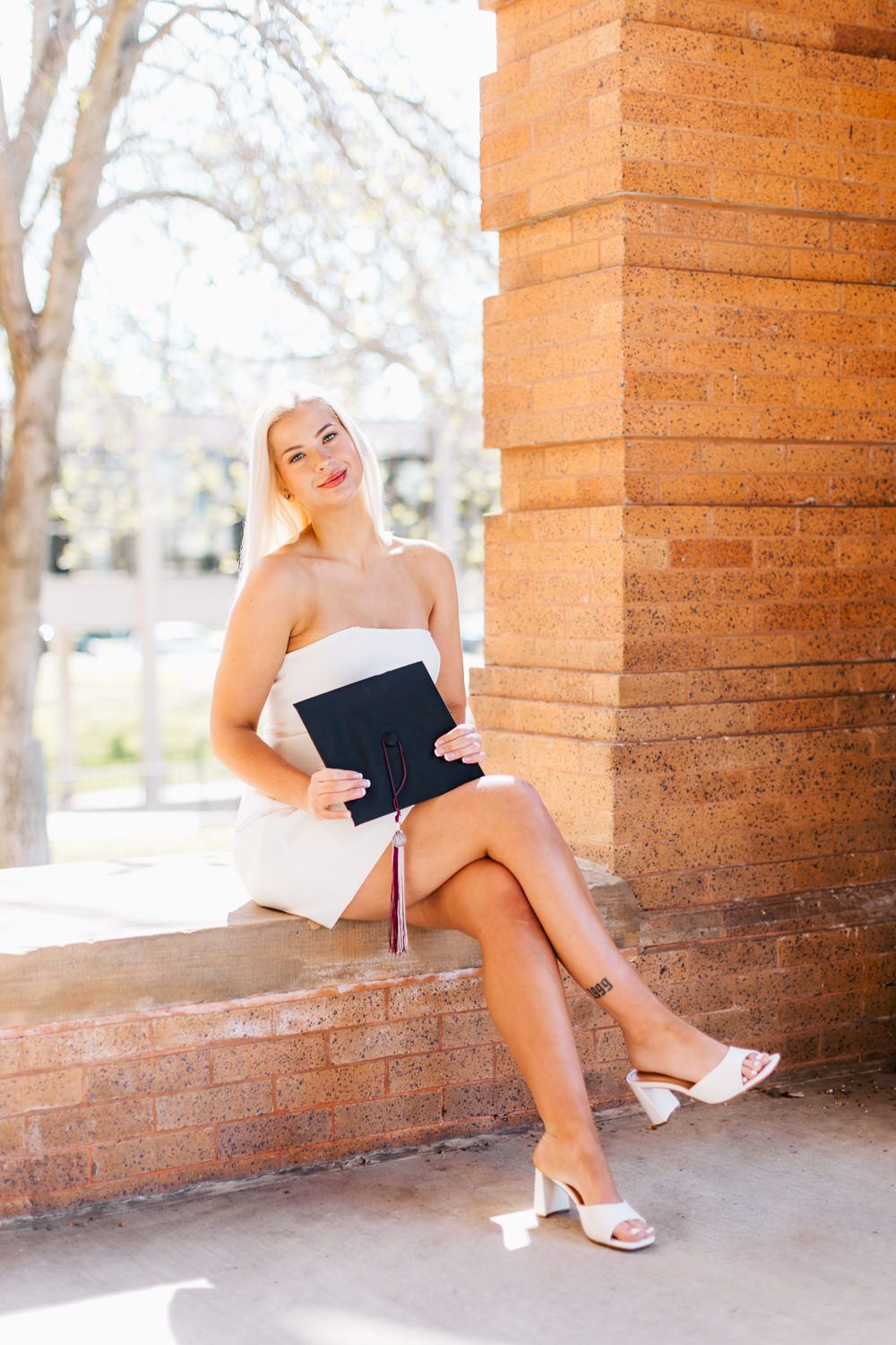 Graduate in white dress posing along brick colonnade during photo session.