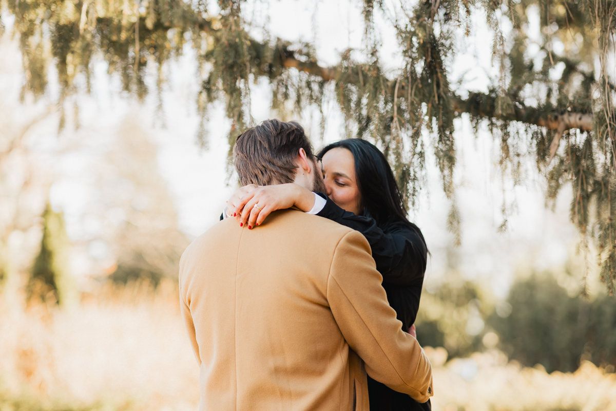 Couple sharing intimate embrace under hanging moss with sunlight streaming through.