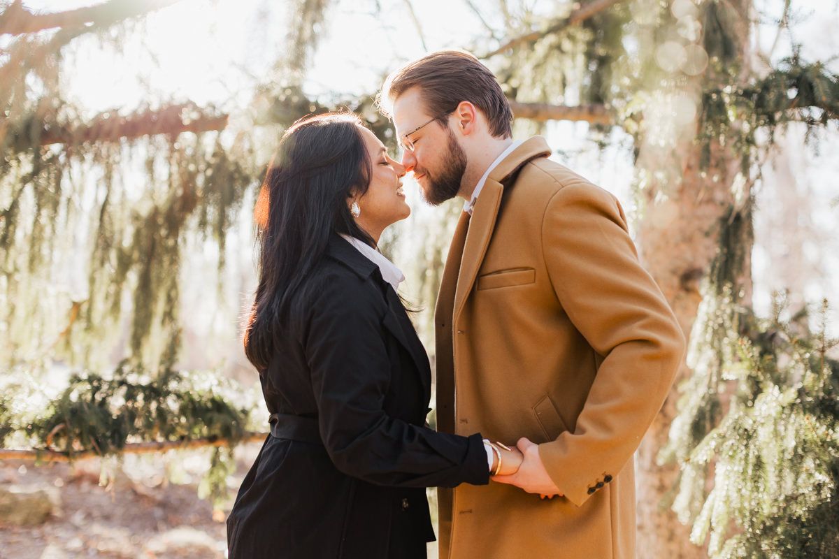 A couple in contrasting coats shares an intimate moment under hanging moss branches.