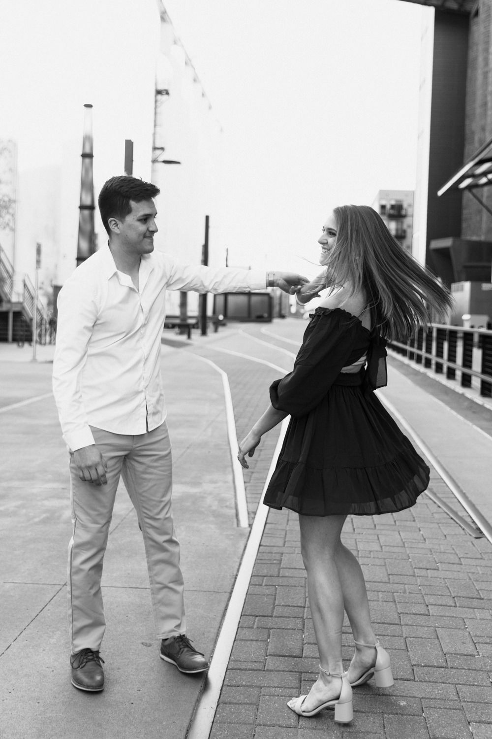 Couple in casual attire sharing playful moment on brick pathway.