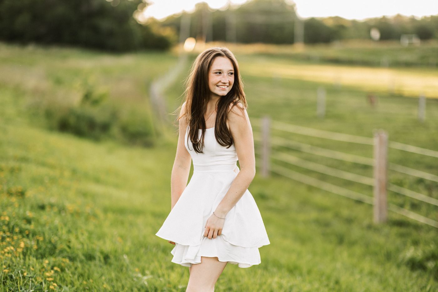 A breezy summer portrait in a white dress against rolling green fields.