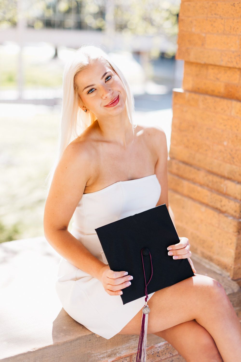 Graduation portrait session with diploma holder against warm brick backdrop.