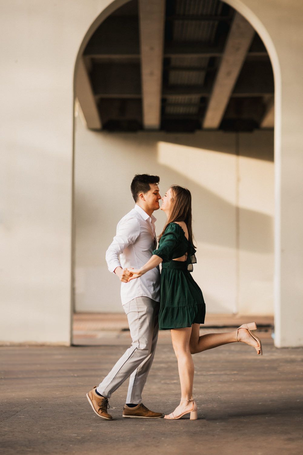 Playful couple in a covered walkway with arched architecture and warm lighting.