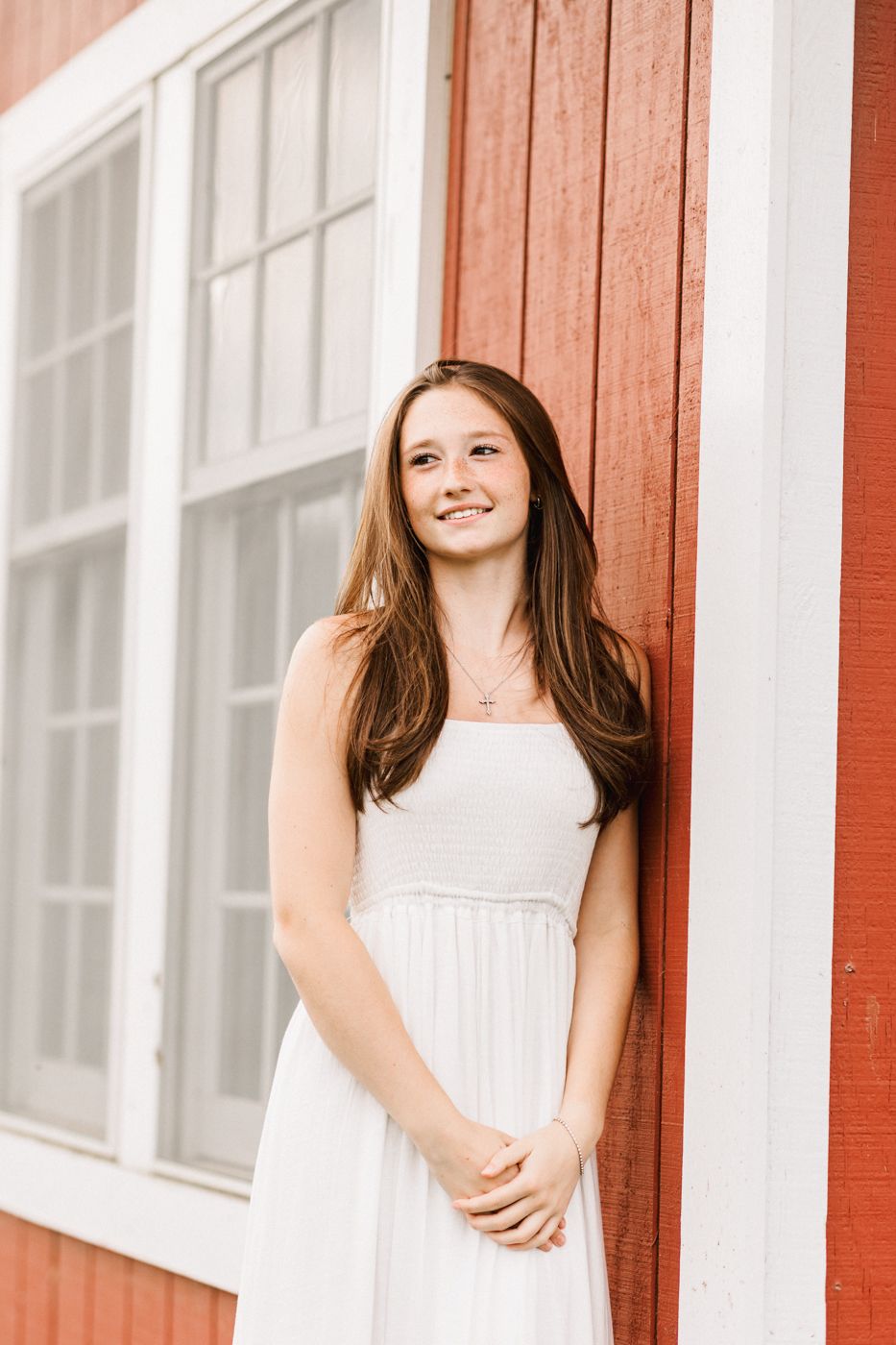 A sunny portrait against a red barn with white trim windows.