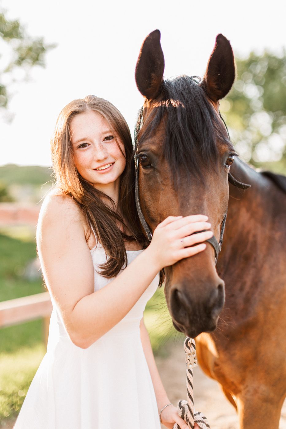 A close-up portrait of a bay horse and a figure in white sharing an affectionate moment outdoors.