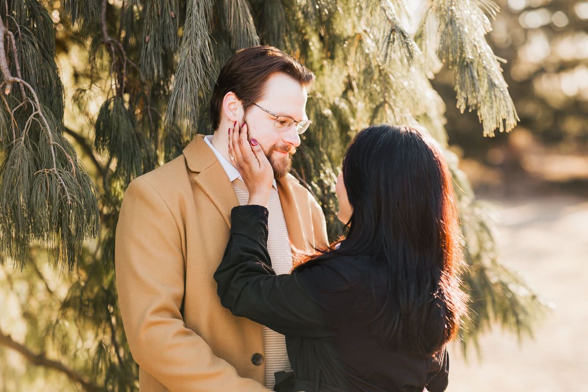 Intimate moment between couple under willow tree branches in warm sunlight.