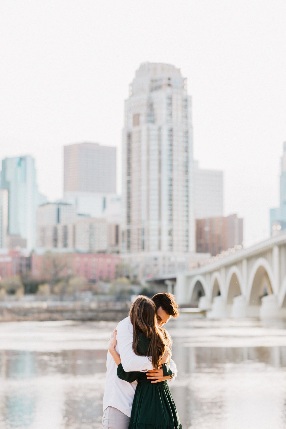 Romantic riverfront scene with couple silhouetted against city buildings and stone arch bridge.
